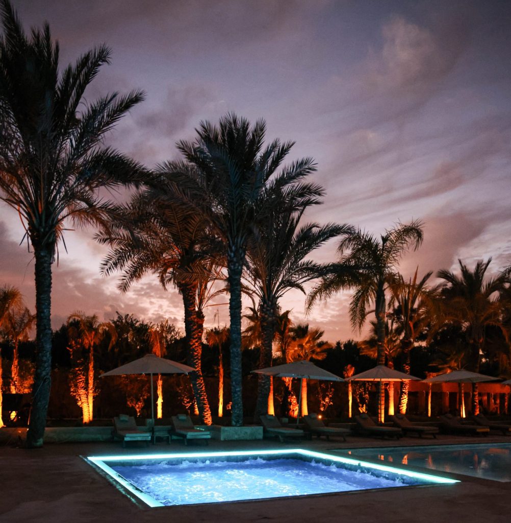 Pool and terrace lit at dusk surrounded by palms